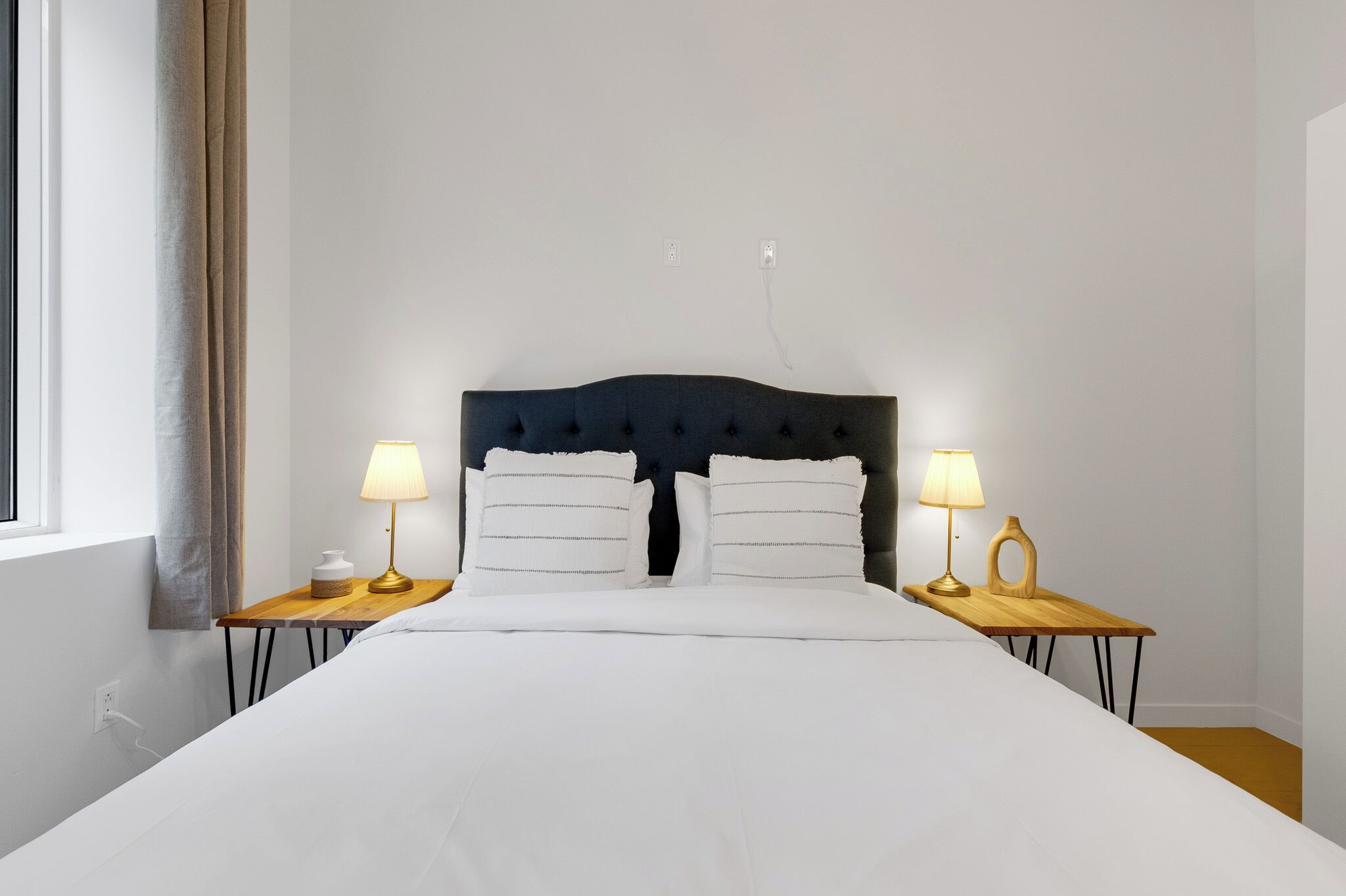A neatly made bed with white linens, two bedside lamps, and a dark headboard.