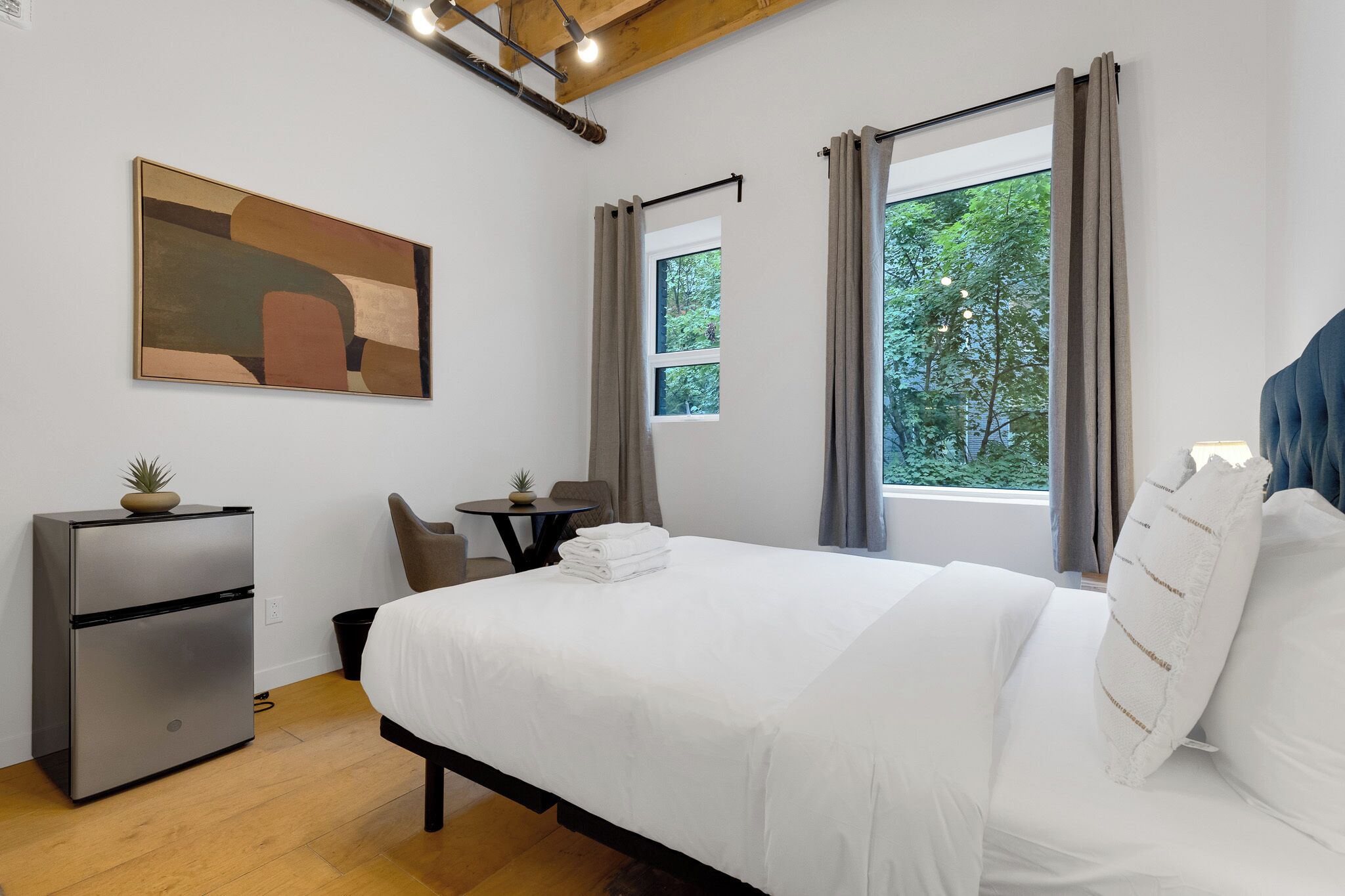 Une chambre d’hôtel moderne, équipée d’un lit, d’un bureau, d’une chaise, d’une petite table avec une plante et d’un tableau au mur.