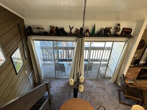 A room with a large sliding glass door leading to an outdoor deck, a dining table with chairs, and a fireplace. - Mammoth Loft | King Bed + 2 Baths | Sleeps 4 (Mammoth Lakes)