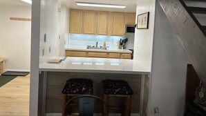 A compact kitchen with wooden cabinets, a white countertop, and a small dining area with two stools. - New Remodeled Studio-Loft Convenient to Town & Bus (Mammoth Lakes)