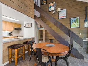 A wooden interior with a dining table, chairs, a kitchen area, and a staircase.