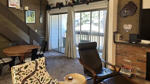 A cozy living room with a fireplace, a large window with curtains, a dining table, and a comfortable chair. - New Remodeled Studio-Loft Convenient to Town & Bus (Mammoth Lakes)