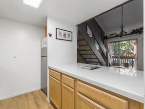 A kitchen with wooden cabinets, a white countertop, and a view of the outdoors through a window.