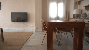 A dining area with a wooden table and wicker chairs, a flat-screen TV mounted on the wall, and a window with white curtains. - 170 Tarek Puerto (Tarifa)