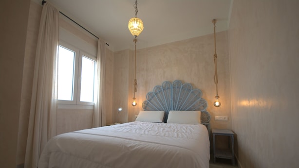 A bedroom with a large bed, a decorative headboard, bedside tables, and a hanging light fixture. - 170 Tarek Puerto (Tarifa)