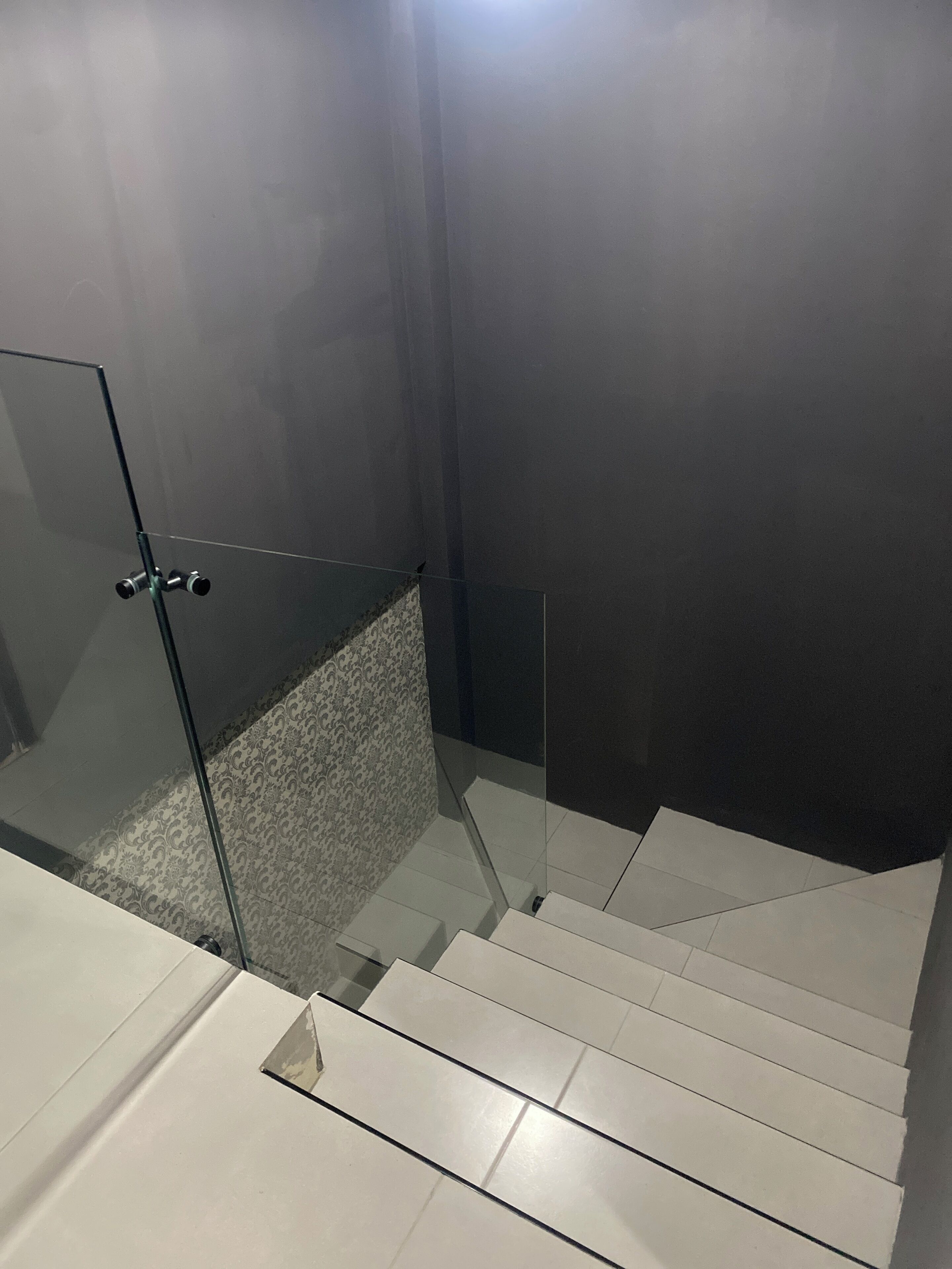 Un baño moderno con cabina de ducha de vidrio, piso estampado y una escalera que conduce a un nivel superior.