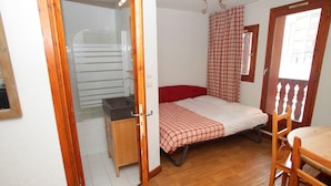 A small room with a bed, a wooden table, and a kitchenette. - Studio abordable - Proche du funiculaire ! (Tignes)