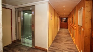 A hallway with wooden paneling, a glass elevator, and a wooden floor. - Studio abordable - Proche du funiculaire ! (Tignes)