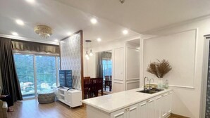 A modern kitchen with a large island, white cabinetry, and a view of the city through large windows. - Halo Bay Retreat (Hong Gai)