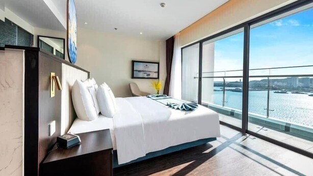 A modern hotel room with a large bed, a desk, and a view of the water. - Halo Bay Retreat (Hong Gai)