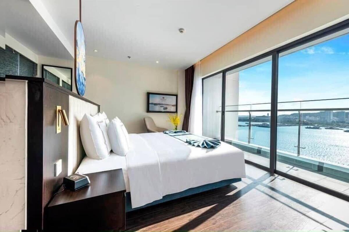 A modern hotel room with a large bed, a desk, and a view of the water.