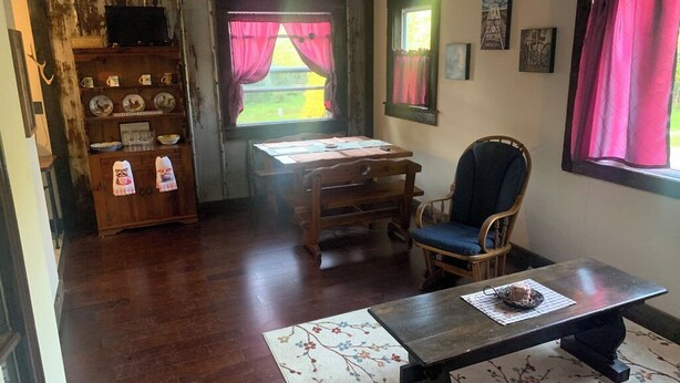 A cozy room with a wooden desk, a chair, a table with a cake, and a shelf with dishes and a television.