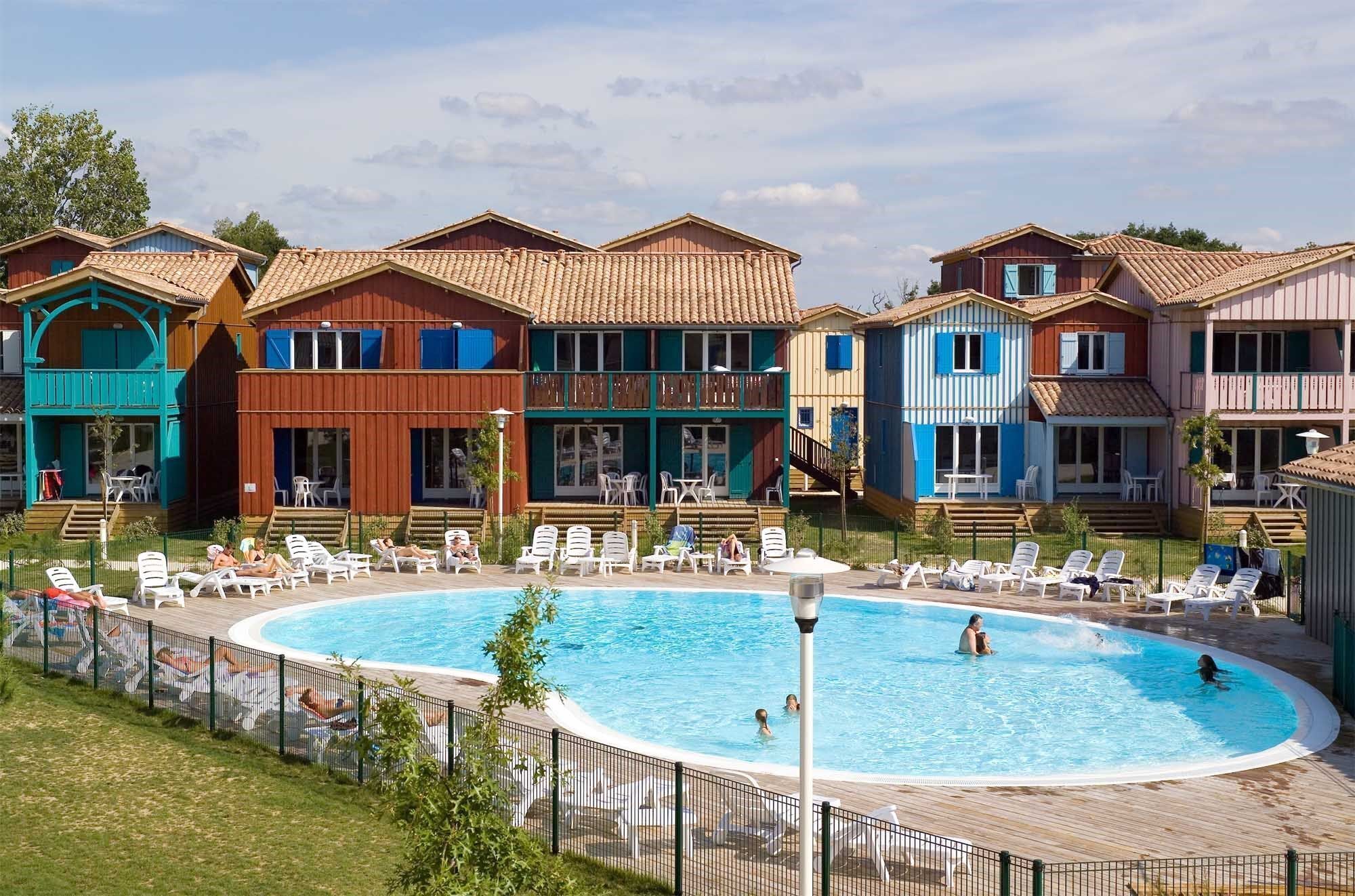 A pool area with multiple colorful buildings, a fenced pool, and lounge chairs.