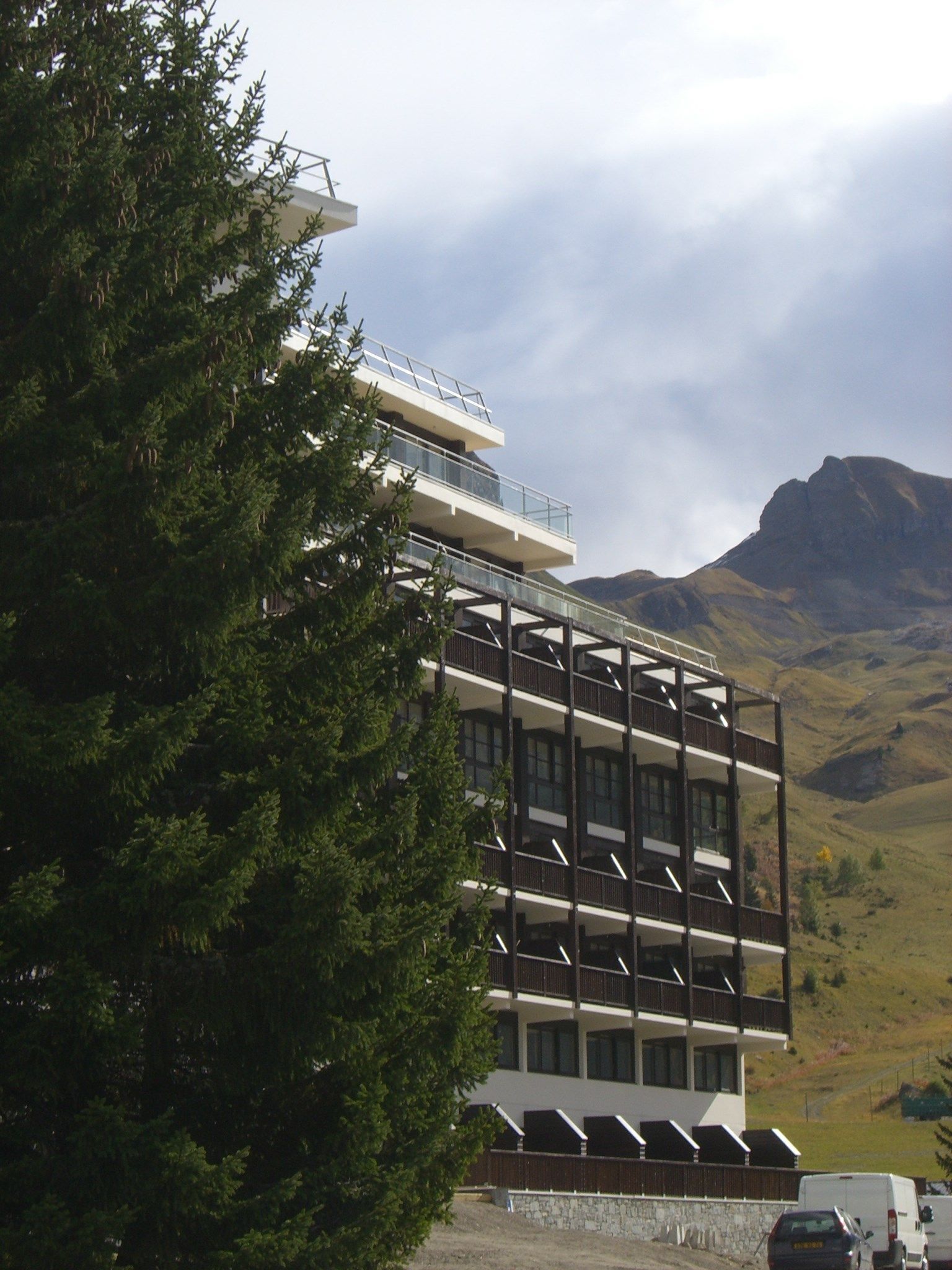 A multi-story hotel with balconies, set against a mountainous backdrop.
