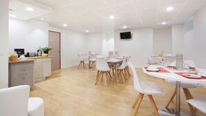 Un espace repas moderne avec des chaises blanches, une table ronde et un comptoir de cuisine doté d’un évier et d’une plante.