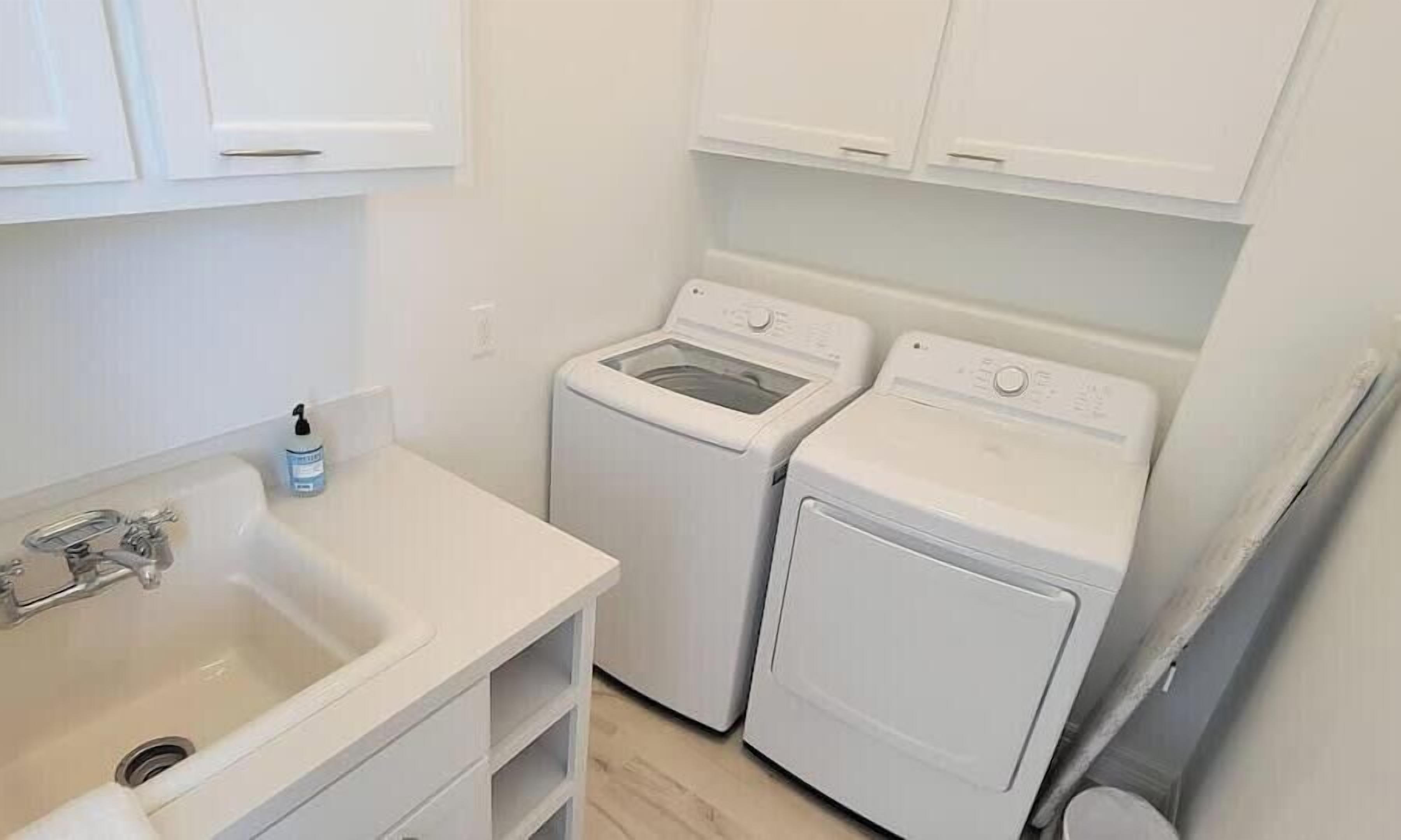A compact laundry room with a sink, two washing machines, and a small bottle of soap.