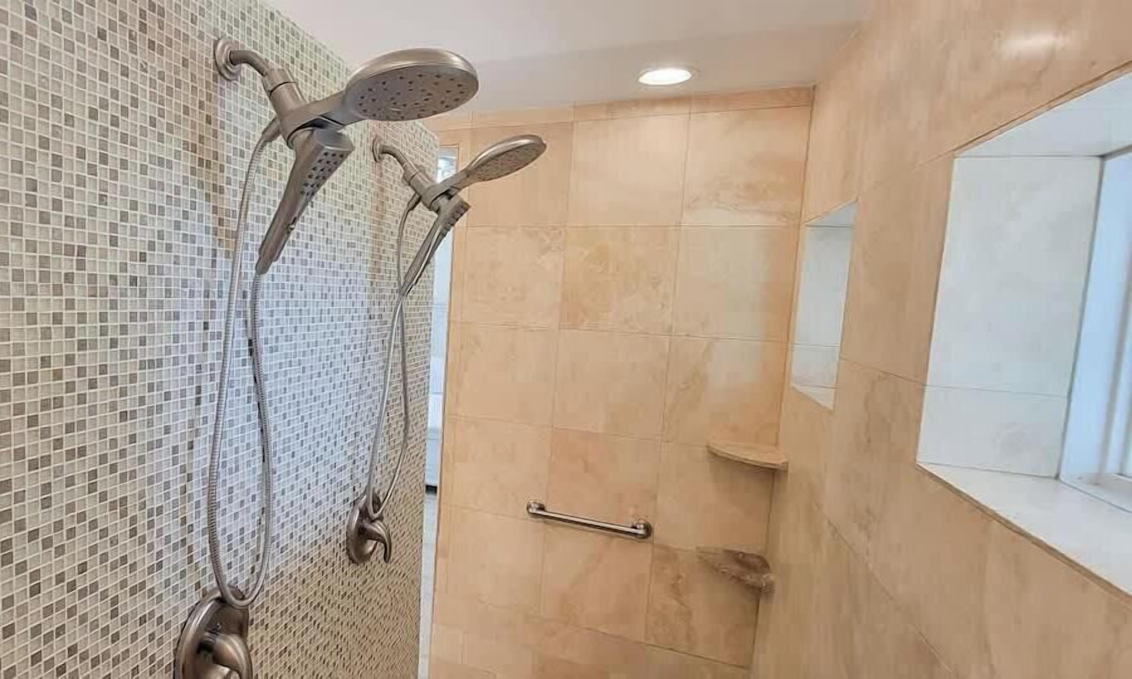 A bathroom with a shower area featuring a mosaic tile wall and a beige tiled floor.