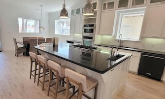 A modern kitchen with a large island, bar stools, pendant lighting, and built-in appliances.