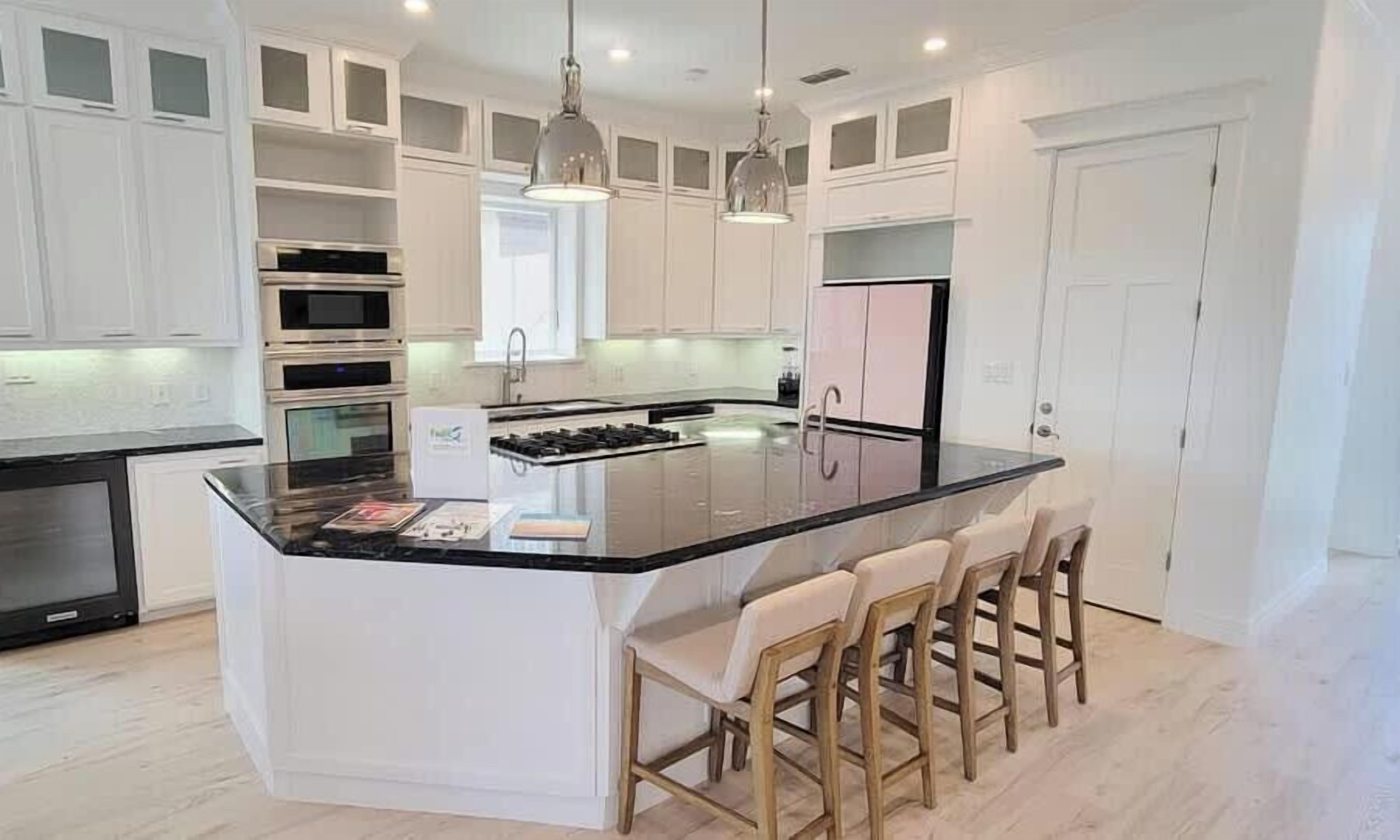 A modern kitchen with white cabinetry, a central island with bar stools, and built-in appliances.