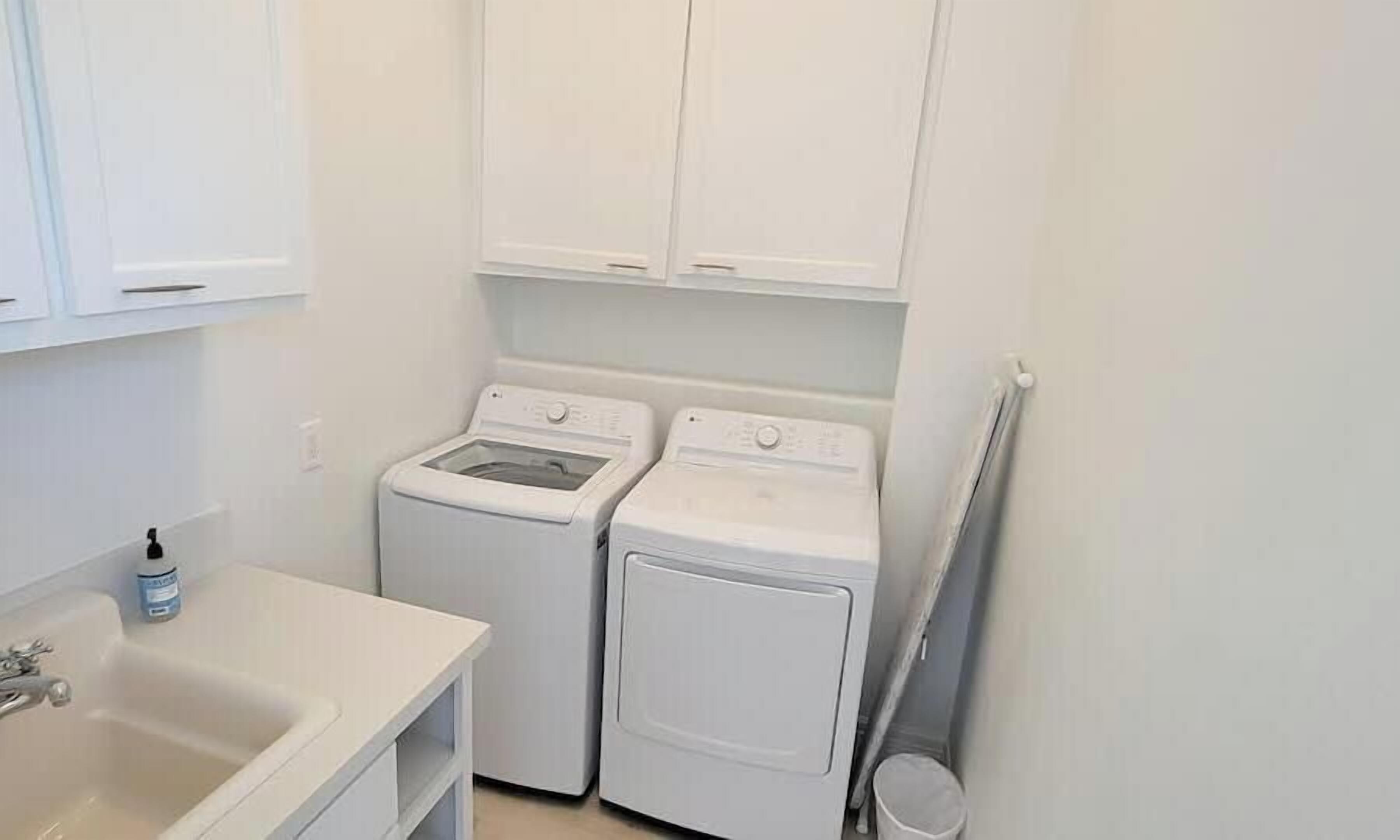 A laundry room with two washing machines, a sink, and cabinets.