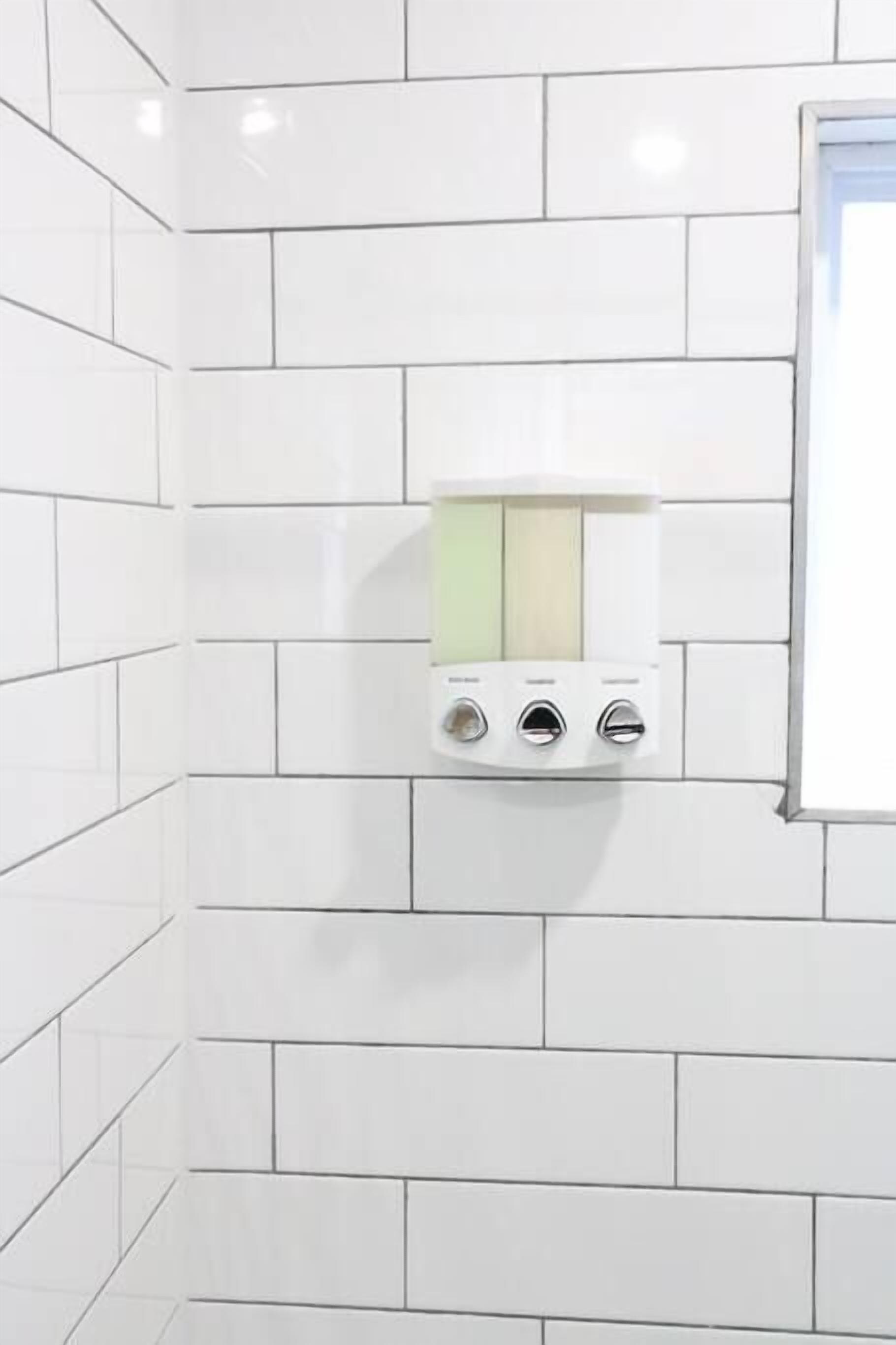 A bathroom with white subway tiles, a white towel dispenser, and a mirror.