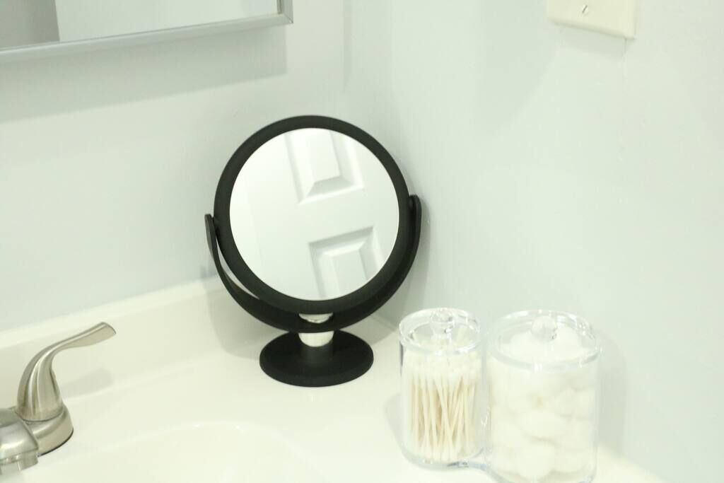 A bathroom with a round mirror, a faucet, and two containers with cotton swabs.