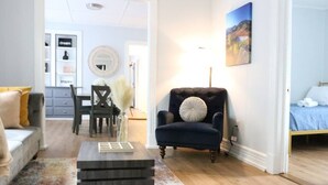 A living room with a dark armchair, a coffee table, a sofa, and a painting on the wall. - 4 bedroom parking ,washer & dryer Apt (New York)