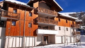 Un edificio de madera de varios pisos, con balcones, un techo nevado y montañas al fondo.