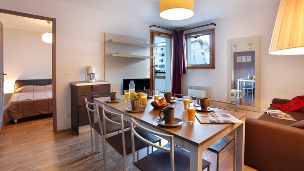 Una habitación de hotel moderna con comedor, cama, escritorio y baño visible a través de una puerta abierta.