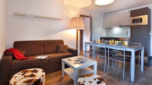 Un espacio habitable compacto con sofá, una mesa de centro, una mesa de comedor con sillas, una lámpara y una kitchenette con microondas.