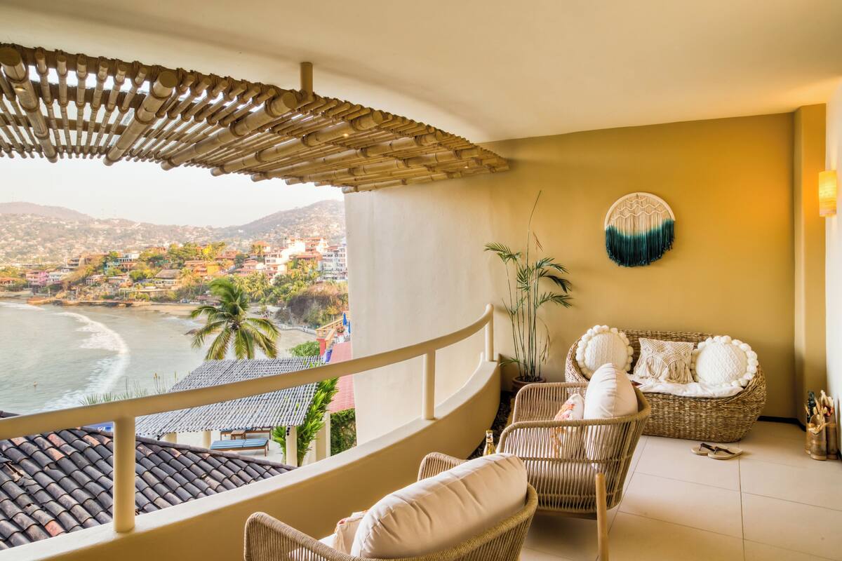 Un balcón con muebles de mimbre, un adorno en la pared y vista al océano y edificios.