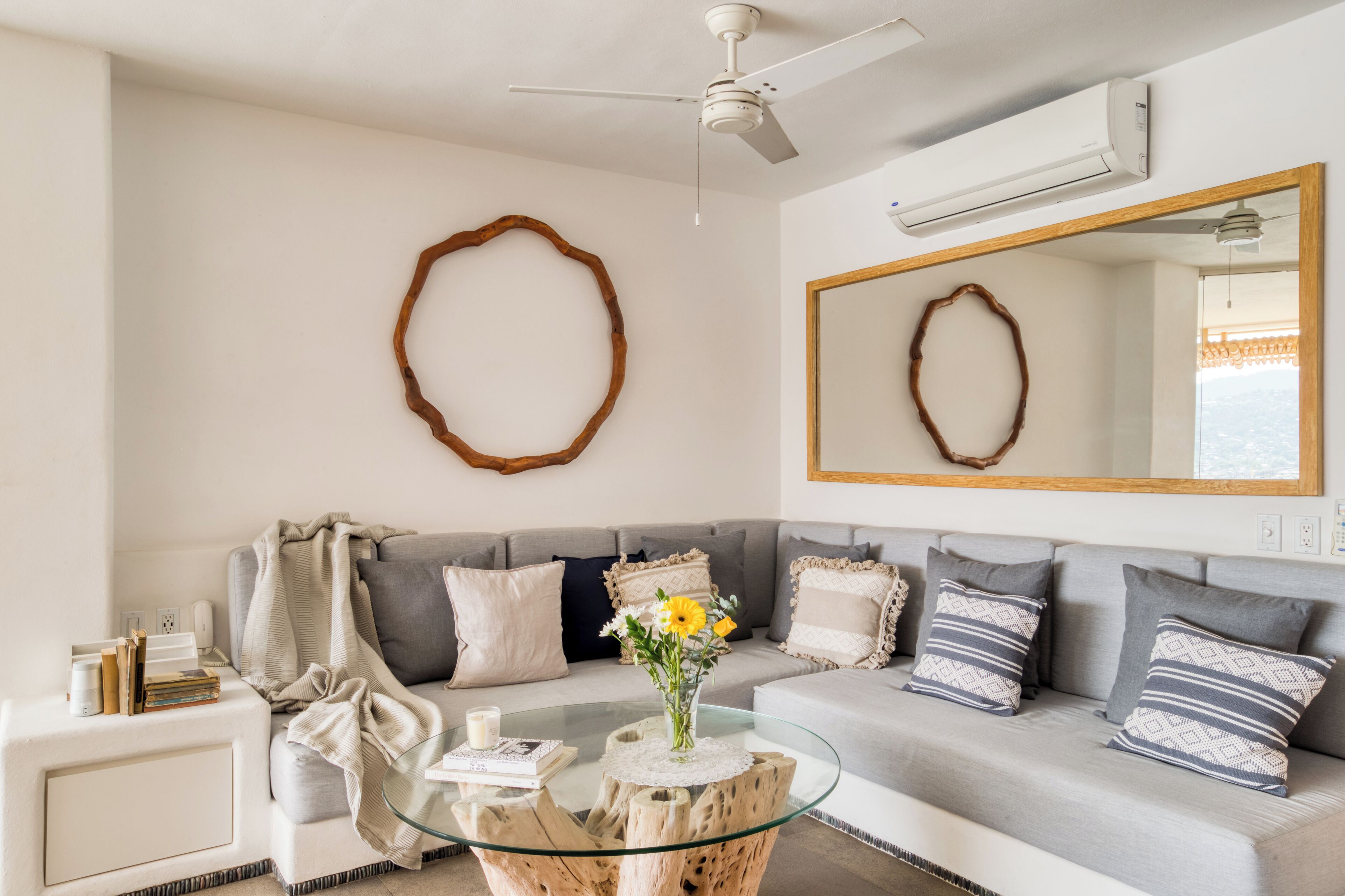 Ein Wohnzimmer mit grauem Sofa, einem Glastisch und einem Holznachttisch.