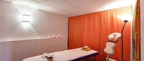 A massage therapy room with a massage table, a headrest, and candles on the wall.
