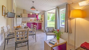 Une cuisine moderne avec des meubles roses, un coin repas avec des chaises blanches et un espace salon confortable avec un fauteuil rouge et une table.