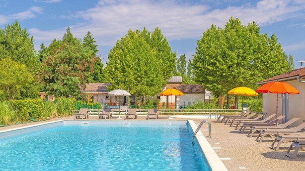 Une piscine entourée d’arbres et de bâtiments, avec des chaises longues et des parasols.