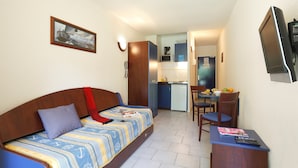A compact room with a bed, a desk, a chair, a microwave, and a small kitchenette. - Studio sur les Rives de l'Ardèche (VALLON-PONT-D’ARC)