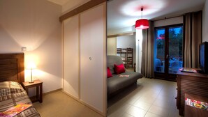 A hotel room with a bed, a sofa, a desk, and a sliding door leading to a balcony.
