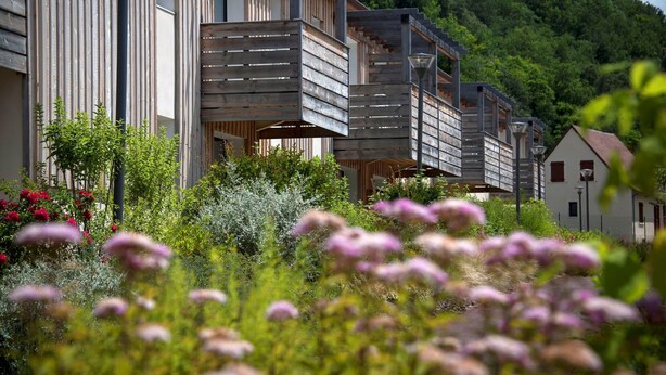 A modern building with a wooden facade and balconies overlooking a lush garden.