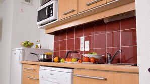 Cocina funcional con microondas, estufa y pileta. Hay frutas y verduras en la encimera, y un escurreplatos sobre la estufa.