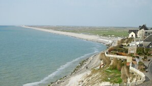 Una zona costiera con spiaggia, una strada che conduce a una scogliera con edifici, e una vista limpida sul mare.