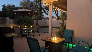 Ein Terrassenbereich im Freien mit Feuerstelle, Stühlen und überdachtem Sitzbereich mit Lichterkette.