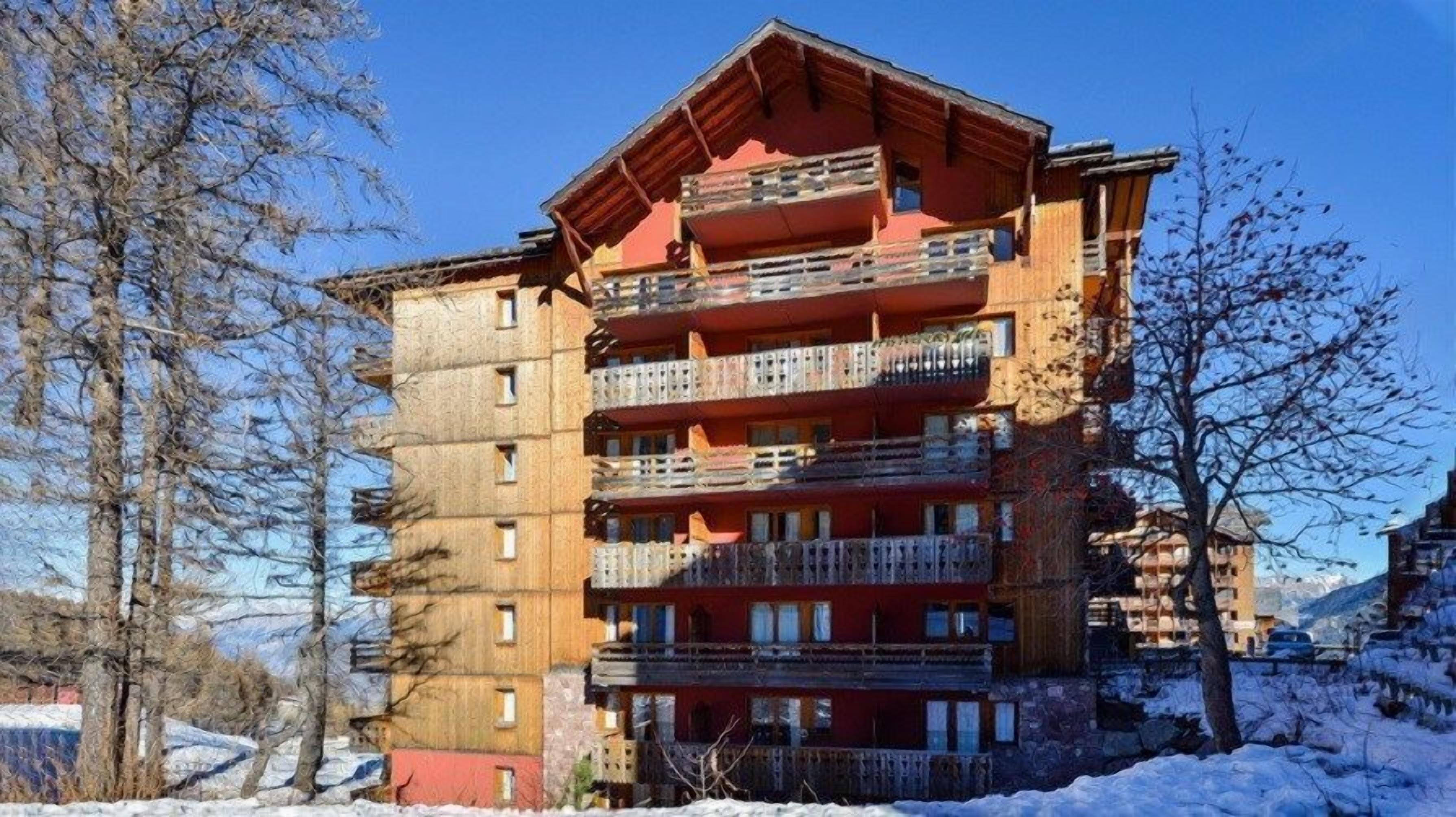 A multi-story hotel with balconies and a ski slope in the background.
