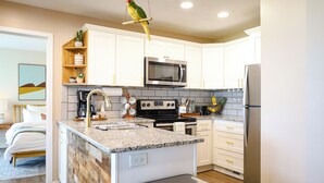 Una cocina moderna con armarios blancos, encimera de granito, refrigerador de acero inoxidable y microondas.