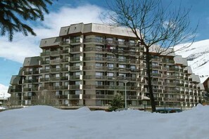 Ein mehrstöckiges Hotel mit Balkonen, einer flachen Dachterrasse und Blick auf schneebedeckte Berge.