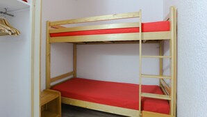 A bunk bed with a red mattress, wooden frame, and a small shelf at the foot of the bed.
