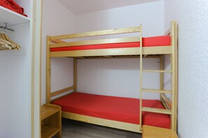 Ein Etagenbett mit roter Matratze, Holzrahmen und einem kleinen Regal unter dem Unterbett.