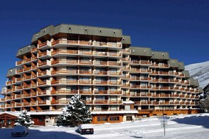 Un hotel a più piani con balconi, una pista da sci sullo sfondo e terreno innevato.
