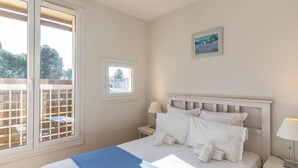 A bedroom with a bed, two bedside tables, a window with blinds, and a small picture on the wall.