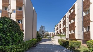 A modern building with a central pathway flanked by neatly trimmed hedges.
