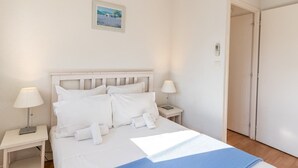 A neatly arranged bedroom with a bed, two bedside tables, a nightstand, a door, and a wall-mounted light switch.